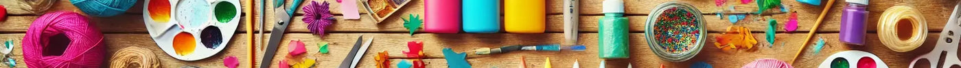Flat lay of colorful craft materials including scissors, glue, paper, paint, and glitter arranged on a wooden table.