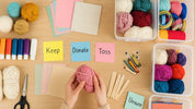 Organized craft supplies on a wooden table with hands sorting yarn and labeled containers for paper, ribbon, and fabric under soft lighting.