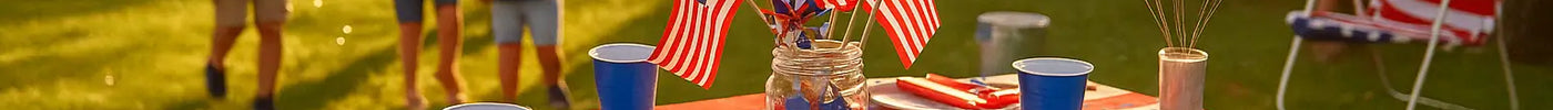 Patriotic backyard party setup with red, white, and blue decor, kids playing, and a festive table at golden hour for 4th of July or Memorial Day celebration.