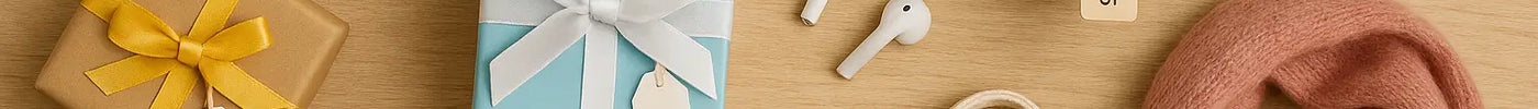 Flat lay of affordable gift ideas under $20, including wrapped presents with price tags, a red coffee mug, teal candle, wireless earbuds, pink scarf, tote bag, pinecones, and gold earrings arranged on a wooden surface.