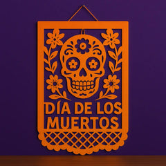 Orange papel picado wall hanging with sugar skull and floral design for Día de los Muertos, perfect Day of the Dead wall decor on purple background.