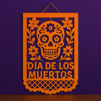 Orange papel picado wall hanging with sugar skull and floral design for Día de los Muertos, perfect Day of the Dead wall decor on purple background.