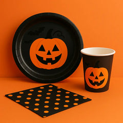 Halloween party supplies with jack-o’-lantern plate, matching cup, and polka dot napkin on orange background—perfect for spooky party table settings.