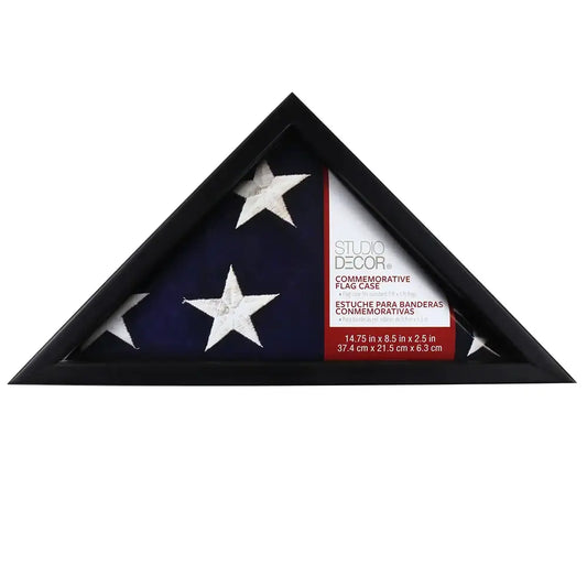 Commemorative flag display case with a black triangular frame, designed to hold a folded American flag. The case features a label indicating it is from Studio Decor. The folded flag inside showcases white embroidered stars on a blue background.