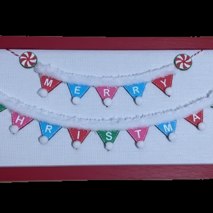 Close-up of colorful Merry Christmas pennant flags with pom-pom garland and peppermint candy accents in red wood frame