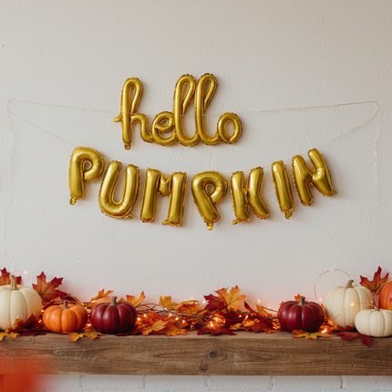 Celebrate It hello PUMPKIN gold foil letter balloon banner hanging on a wall at a Thanksgiving party with pumpkins and fall leaves in the background