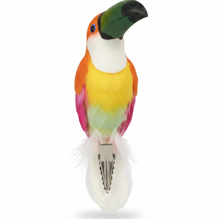 Decorative toucan bird ornament with green beak, orange shoulders transitioning to yellow, pink and white feathers, with alligator clip on white background