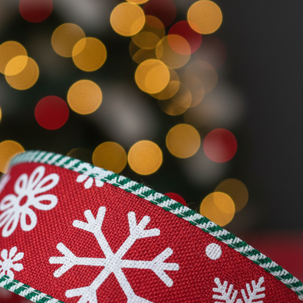 Close up of Celebrate It red wired ribbon showing white snowflake pattern and green striped edge detail with soft Christmas bokeh background
