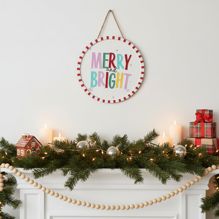 Round Merry and Bright wall sign hung above a Christmas mantel with garland and candles