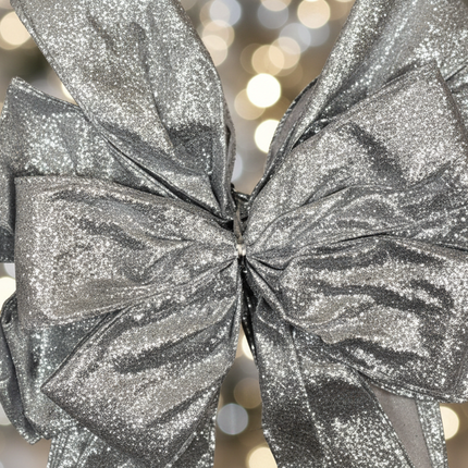 Close up of large silver glitter decorative bow showing sparkle and glitter texture detail with soft bokeh Christmas background
