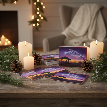 Glory to the Newborn King Christmas cards displayed on rustic wooden table with candles, pine cones, and evergreen branches