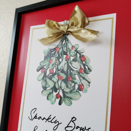 Close-up of watercolor mistletoe illustration with red berries and gold bow accent in framed wall decor