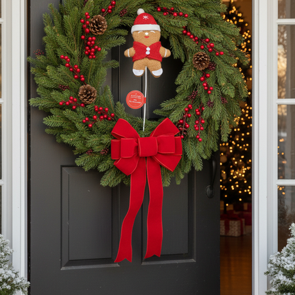 Ashland 12 inch gingerbread man decorative pick inserted into a Christmas wreath with red ribbon and pine cones on a front door