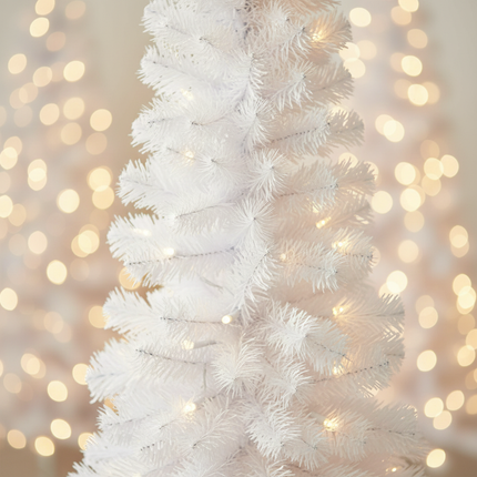 Close-up of white pencil Christmas tree branches with warm white pre-lit lights glowing