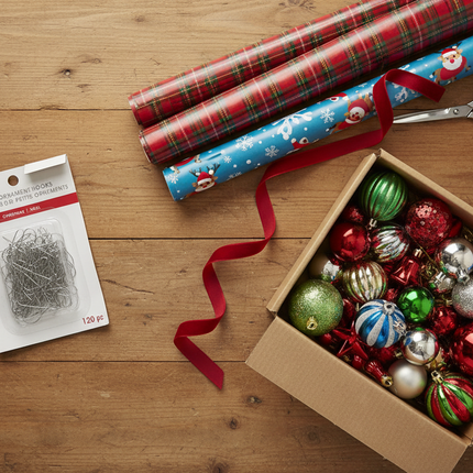 Silver Christmas ornament hooks styled next to a box of assorted Christmas ornaments and gift wrap on a wooden table