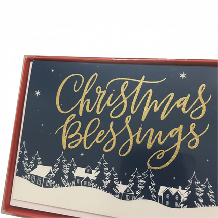 Close-up of Christmas Blessings card showing gold foil script lettering on deep navy blue starry sky with white snow village and pine trees