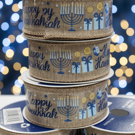 Close up of Celebrate It Happy Hanukkah wired burlap ribbon showing menorah dreidel gift boxes and gold coin motifs in blue and gold with soft blue bokeh Hanukkah candle background